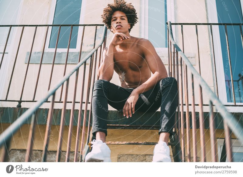 ein junger schwarzer Mann ohne Hemd, der in der Treppe sitzt. Jugendliche Athlet nackt Torso Mensch Person gemischter Abstammung Afro-Look krause Haare