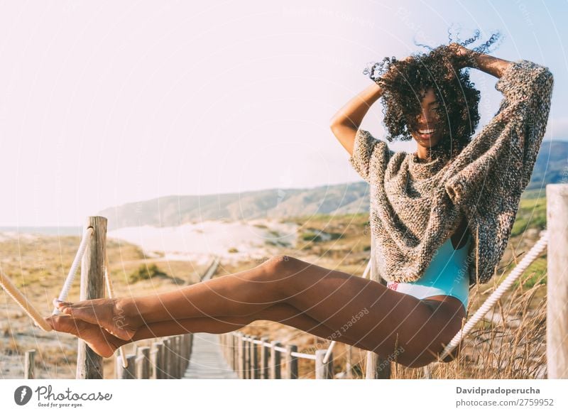 Schöne junge schwarze Frau, die in einer hölzernen Fußgängerbrücke am Strand sitzt. Hintergrundbild Bikini Brücke Küste krause Haare Ausflugsziel Behaarung