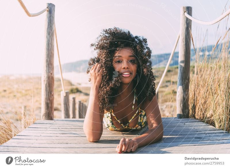 Schöne junge schwarze Frau, die in einer hölzernen Fußgängerbrücke am Strand liegt. Hintergrundbild Bikini Brücke Küste krause Haare Ausflugsziel Mädchen