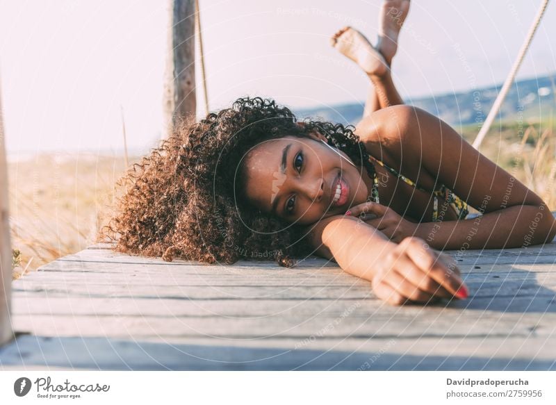 Schöne junge schwarze Frau, die in einer hölzernen Fußgängerbrücke am Strand liegt. Hintergrundbild Bikini Brücke Küste krause Haare Ausflugsziel Mädchen