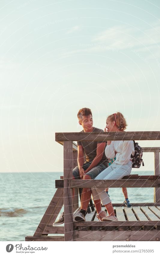Lächelnde junge Frau und Mann, die auf einem Pier über dem Meer sitzen. Lifestyle Freude Glück Freizeit & Hobby Ferien & Urlaub & Reisen Sommer Mensch Junge