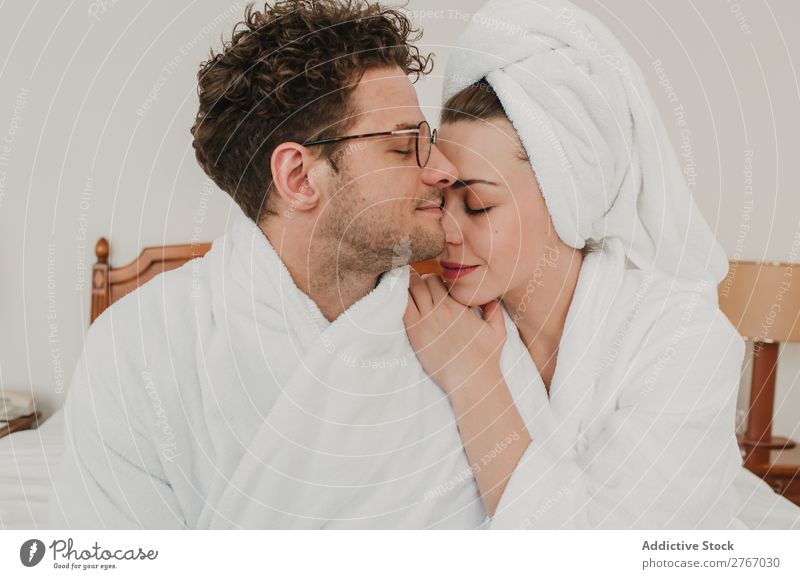 Ein glückliches Paar, das sich auf dem Bett umarmt. Bademantel umarmend Kuscheln Augen geschlossen Hotel Raum Schlafzimmer heimwärts Innenarchitektur Möbel