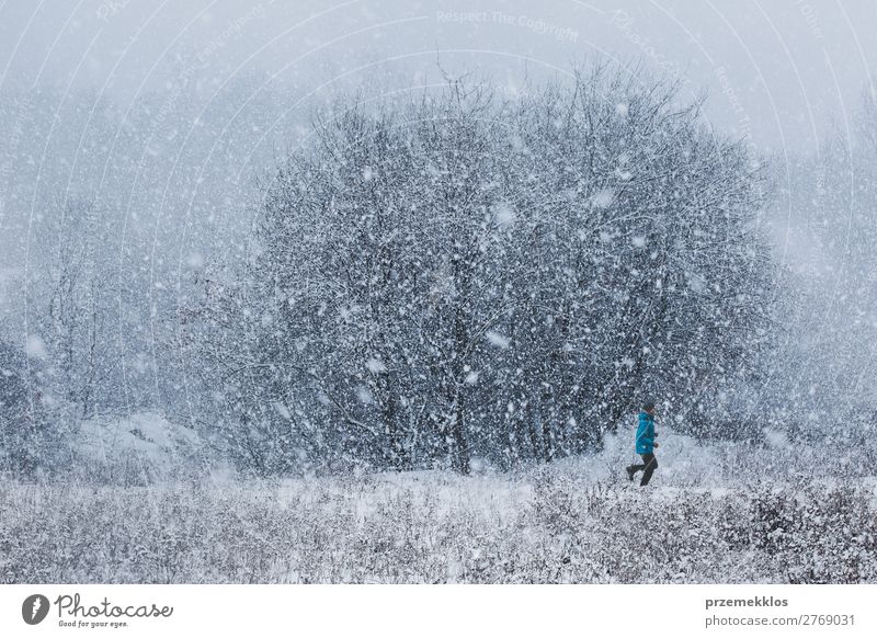 Junger Mann joggt bei starkem Schneefall durch den Wiesenweg. Training im Freien während Schneesturm im Winter Lifestyle Erholung Freizeit & Hobby Sport Joggen
