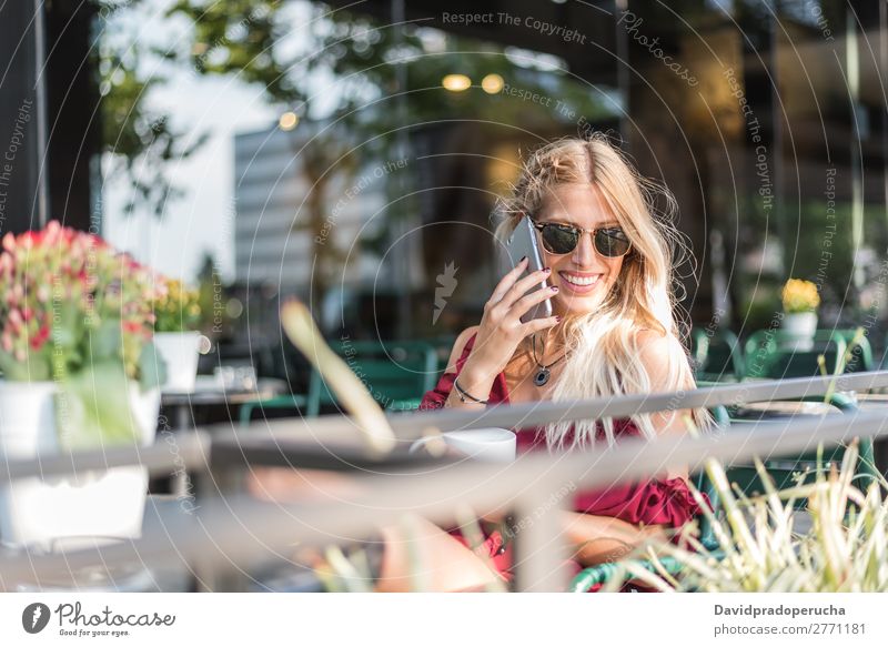Glückliche blonde schöne Frau mit einem Handy, die eine Tasse Kaffee auf der Terrasse trinkt. Lächeln PDA Sonnenbrille Restaurant Kantine Schüler vereinzelt
