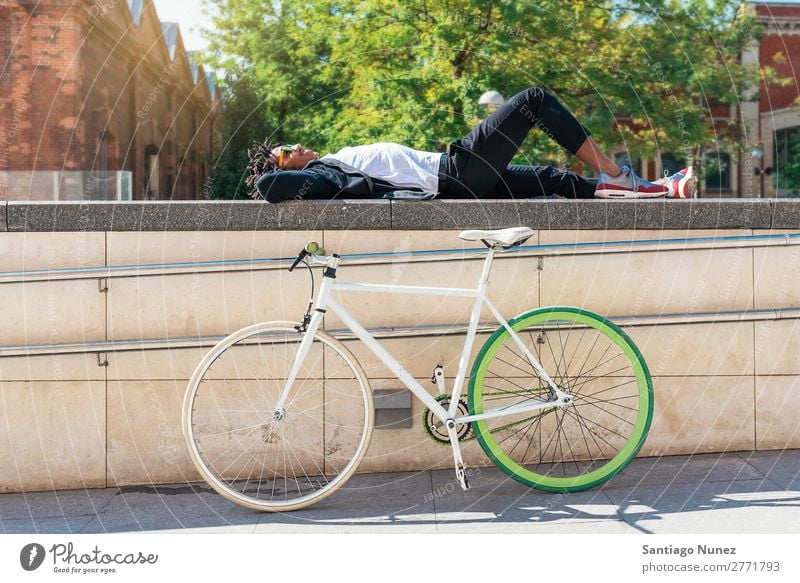 Ein gutaussehender Afro-Mann, der sich in der Nähe seines Fahrrads entspannt. Fixie Schickimicki Lifestyle aussruhen lügen Erholung genießend Fahrradfahren