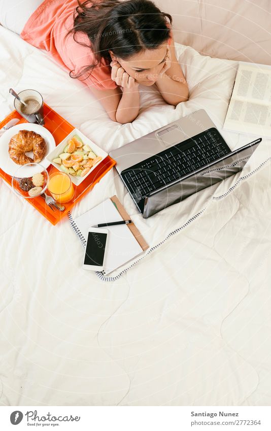 Frau, die den Laptop beobachtet und frühstückt. Frühstück Bett Notebook Kaffee Frucht Saft Orangensaft Croissant Ernährung Arbeit & Erwerbstätigkeit