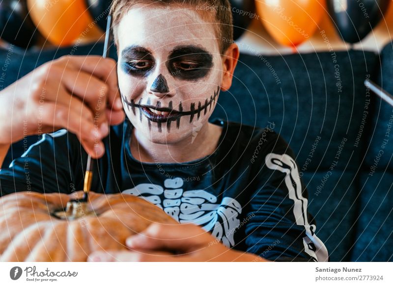 Ein fröhlicher Junge verkleidet, der zu Hause einen Kürbis schmückt. Halloween Kind malen Skelett Freude Familie & Verwandtschaft Hermano Porträt Angst