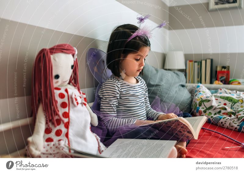 Mädchen verkleidet als Schmetterling, liest mit ihrer Puppe. Lifestyle schön Spielen lesen Lampe Schlafzimmer Kind Mensch Frau Erwachsene Freundschaft Kindheit