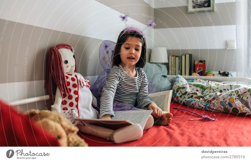 Verkleidetes kleines Mädchen sitzt auf dem Bett und bringt einer Puppe das Lesen bei Lifestyle schön Spielen lesen Lampe Schlafzimmer Kind Mensch Frau