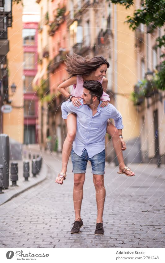 Glückliche Freundin, die auf den Rücken ihres Freundes auf der Straße springt. Paar Huckepack springen Bewegung heiter Lächeln Freude Gefühle vertikal Tag