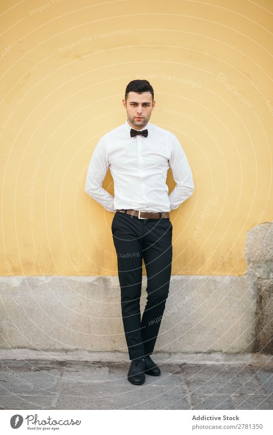 Gut gekleideter Geschäftsmann, der sich auf die gelbe Wand lehnt. 20s Erwachsene Architektur Einstellung Rücken hinten Fliege Business Geschäftsleute Kaukasier