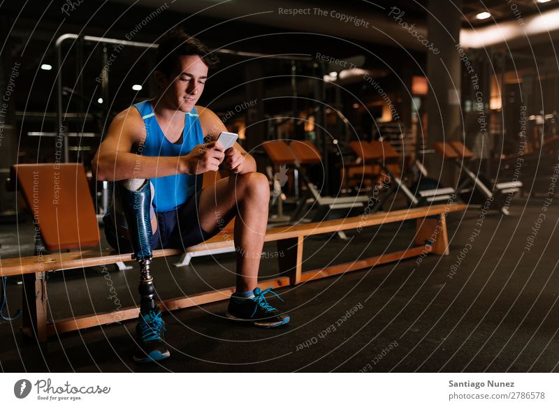 Behinderter junger Mann, der sein Handy in der Turnhalle benutzt. Jugendliche Athlet Sport prothetisch Porträt deaktiviert paralympisch benutzend Mobile Tippen
