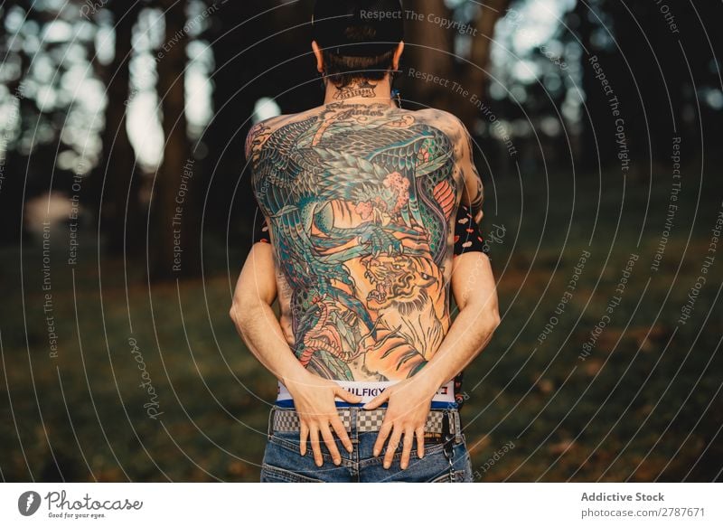 Junger Mann mit Tattoos umarmt die Dame im Wald. Paar Umarmen Schnappschuss Park ohne Hemd Typ Jugendliche Schickimicki umarmend Frau romantisch Kunst