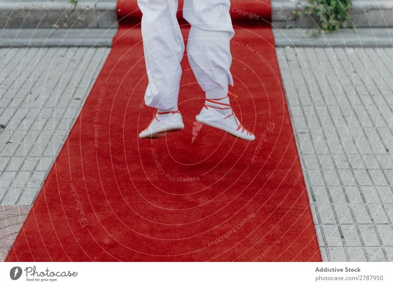 Person in weißem Stoff und Turnschuhen, die auf rotem Teppich springt. Roter Teppich Mensch Anzug springen Beine Straße anhaben Lifestyle Reichtum Erfolg