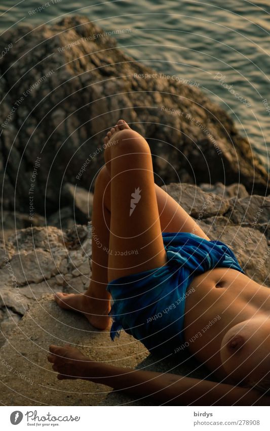 Junge barbusige Frau mit einem Tuch um die Lenden liegt abends lasziv auf einem Felsen an der Adriaküste Lifestyle exotisch Sommerurlaub Frauenbrust Meer