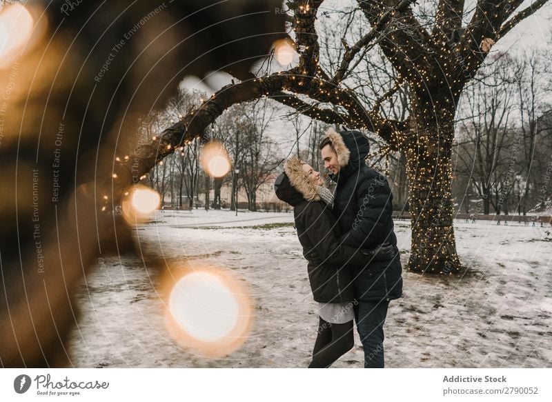 Lächelndes Paar, das Spaß auf der Straße in der Nähe eines Baumes mit Lichterketten hat. Spaß haben Weihnachten & Advent Typ Dame Skijacke Glück Hand Holz