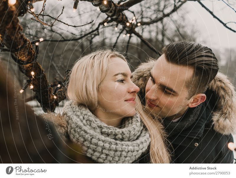 Lächelndes Paar, das Spaß auf der Straße in der Nähe eines Baumes mit Lichterketten hat. Spaß haben Weihnachten & Advent Typ Dame Skijacke Glück