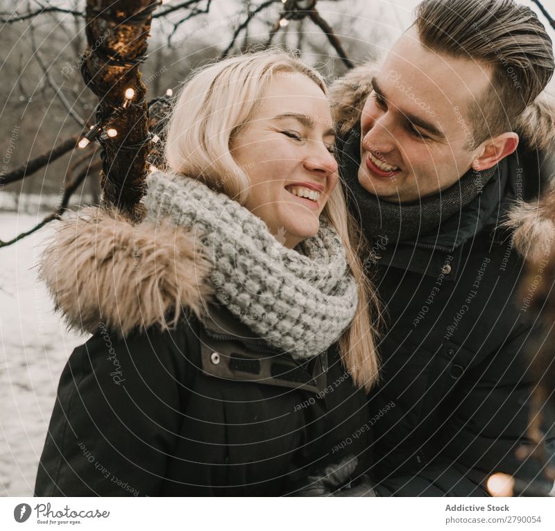 Lächelndes Paar, das Spaß auf der Straße in der Nähe eines Baumes mit Lichterketten hat. Spaß haben Weihnachten & Advent Typ Dame Skijacke Glück lachen Holz