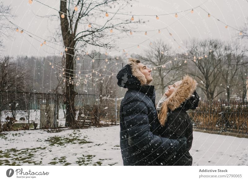 Lächelndes Paar, das Spaß auf der Straße in der Nähe eines Baumes mit Lichterketten hat. Spaß haben Weihnachten & Advent Typ Dame Skijacke Glück Hand Holz