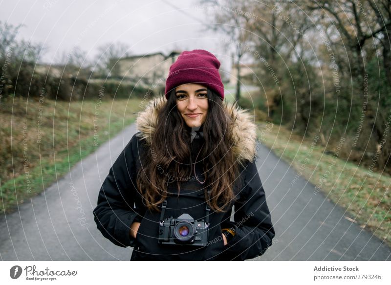 Lächelnde Frau im Mantel mit Kamera Fotokamera Landschaft Orduna Spanien Dame Hut Hand Tasche heiter anhaben Winter attraktiv Jugendliche Straße