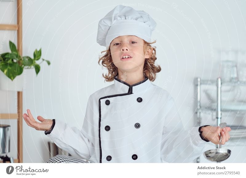 Junge mit Kochmütze, der die Schöpfkelle hält und den Daumen in der Küche zeigt. Schöpflöffel Daumen hoch Küchenchef Kind Hut Coolness gestikulieren