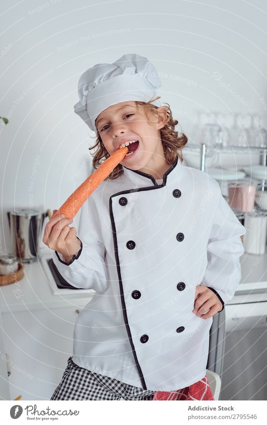 Junge mit Kochmütze mit Karotte in der Küche Möhre Küchenchef Kind Gemüse Hut frisch zeigen Hand Hüfte kochen & garen modern lustig heimwärts Licht vorbereitend
