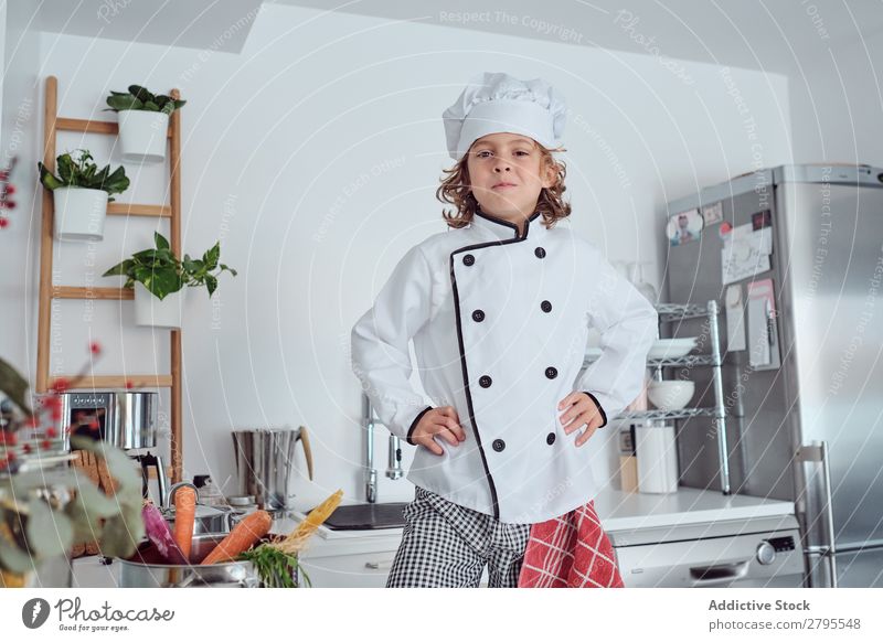 Junge mit Kochmütze in der Küche Möhre Küchenchef Kind Gemüse Hut frisch zeigen Hand Hüfte kochen & garen modern lustig heimwärts Licht vorbereitend