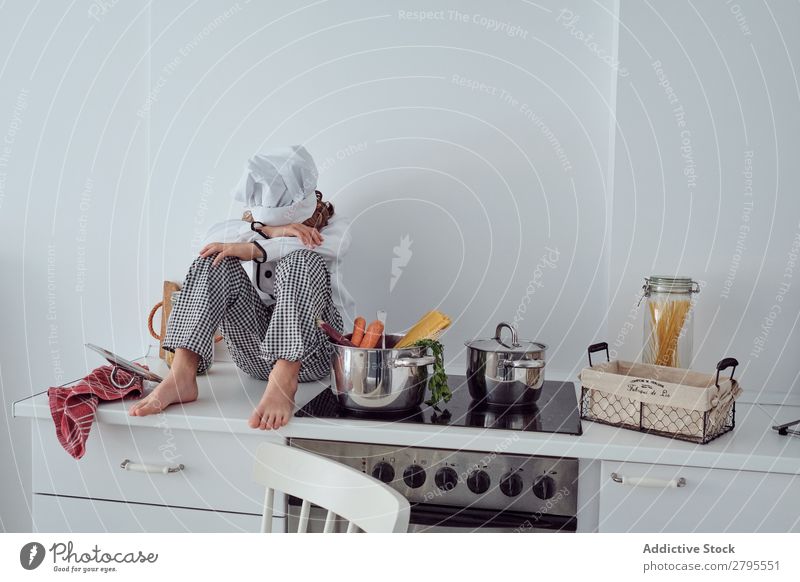 Junge mit Kochmütze neben Töpfen auf der Elektrofritteuse in der Küche sitzend Topf Küchenchef Kind Gemüse Hut Herd & Backofen kochen & garen modern lustig