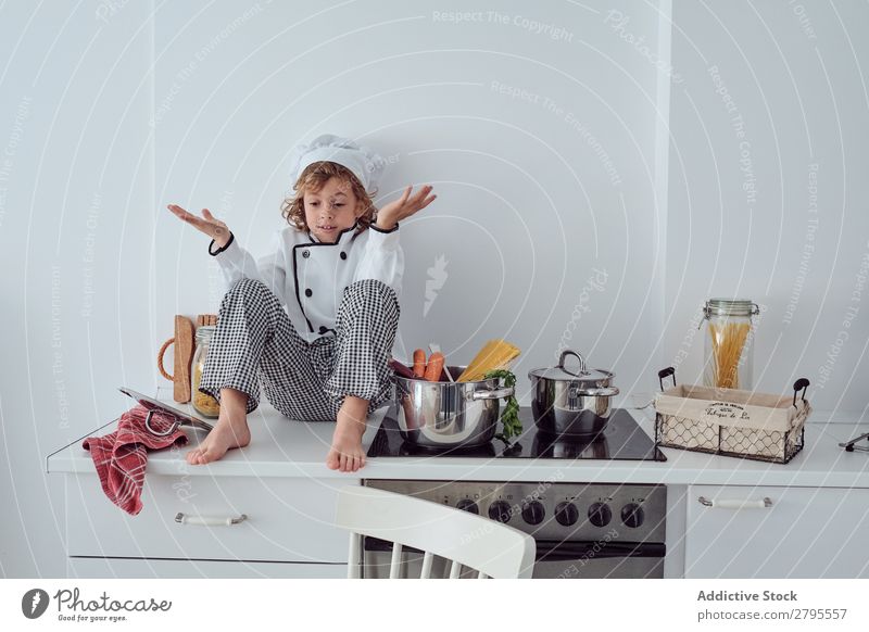 Junge mit Kochmütze neben Töpfen auf der Elektrofritteuse in der Küche sitzend Topf Küchenchef Kind Gemüse Hut Herd & Backofen kochen & garen modern lustig