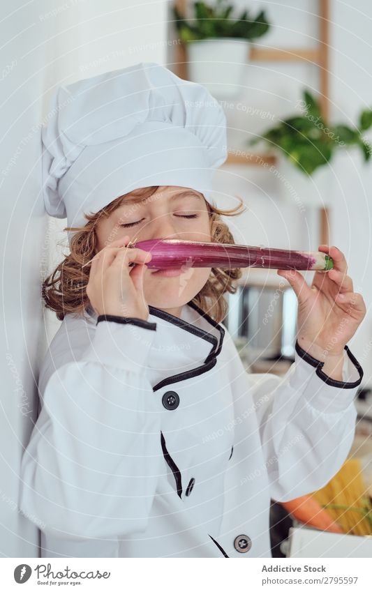 Junge mit Kochmütze mit Gemüse in der Küche Küchenchef Kind Hut riechend geschlossene Augen frisch kochen & garen modern lustig heimwärts Licht vorbereitend