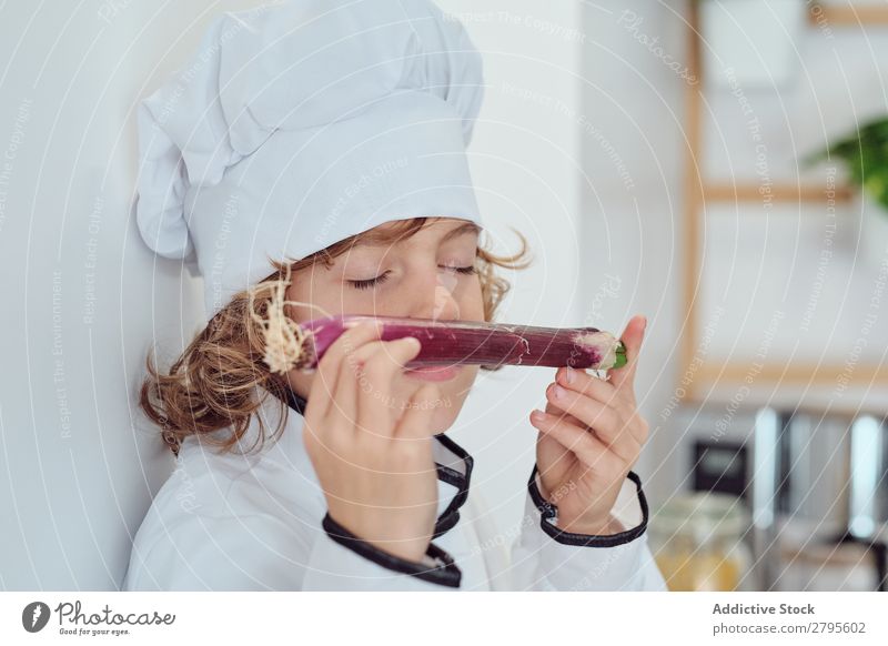 Junge mit Kochmütze mit Gemüse in der Küche Küchenchef Kind Hut riechend geschlossene Augen frisch kochen & garen modern lustig heimwärts Licht vorbereitend