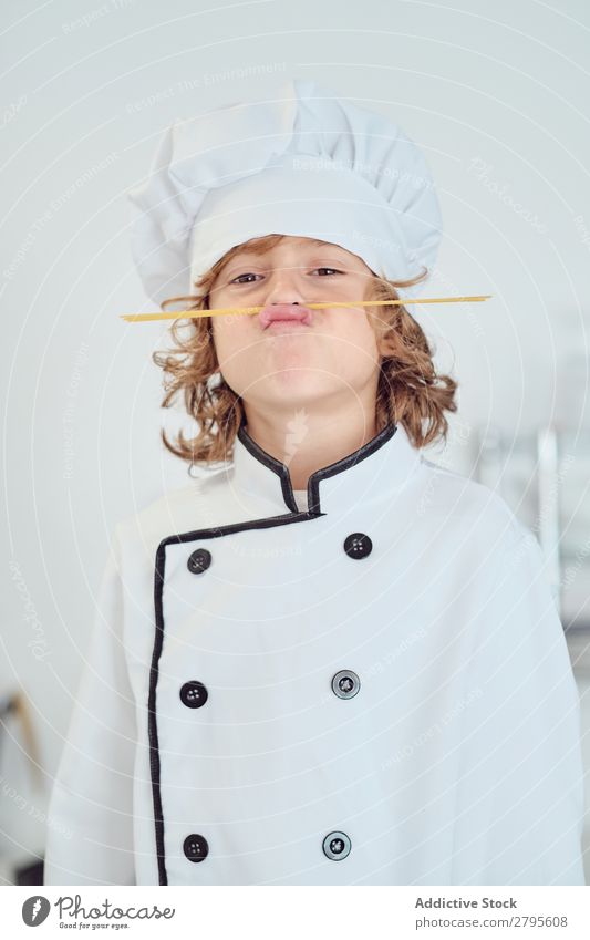 Junge mit Kochmütze, der in der Küche einen Schnurrbart aus Makkaroni macht. Oberlippenbart Küchenchef Kind Hut Spätzle regenarm machen kochen & garen modern