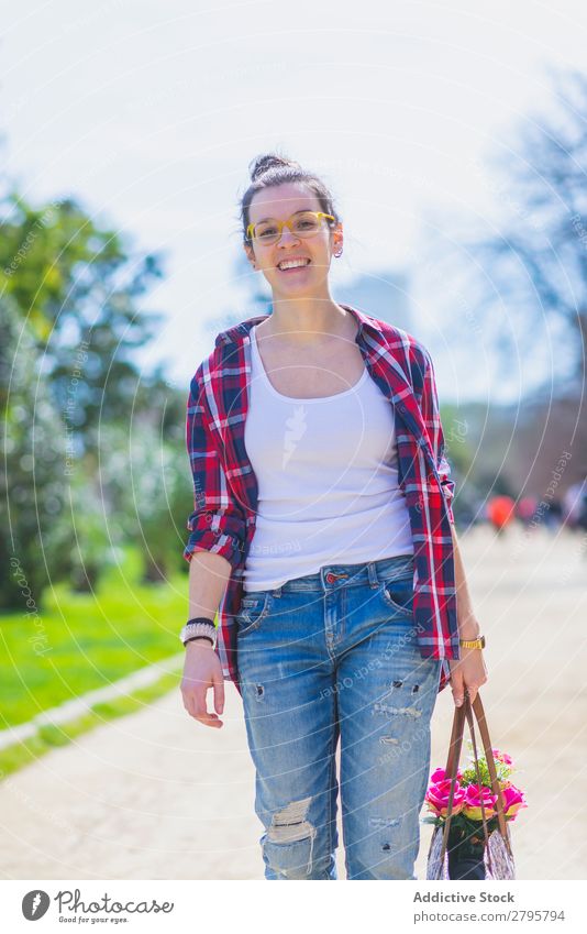 Vorderansicht einer jungen lächelnden Hipsterfrau, die an sonnigen Tagen in einem Park spazieren geht und dabei einen bösen Korb hält. Junge Frau Schickimicki