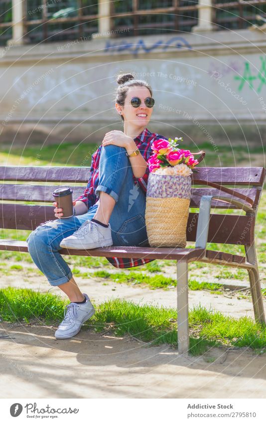Vorderansicht einer jungen Hipsterfrau, die auf einer Parkbank sitzt und sich an einem sonnigen Tag entspannt und dabei wegblickt. Junge Frau Schickimicki