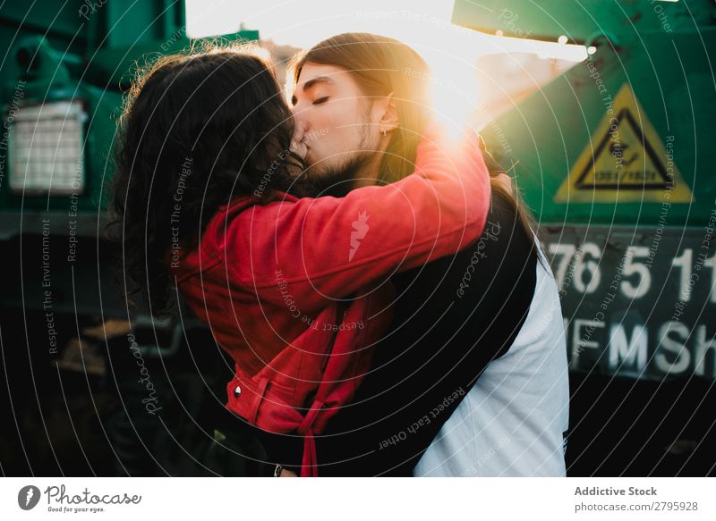 Langhaariger Mann, der die Frau in der Nähe des Zuges umarmt und küsst. Paar Verlassen Waggons Umarmen Eisenbahn Graffiti alter Zug Küssen Liebe Lokomotive