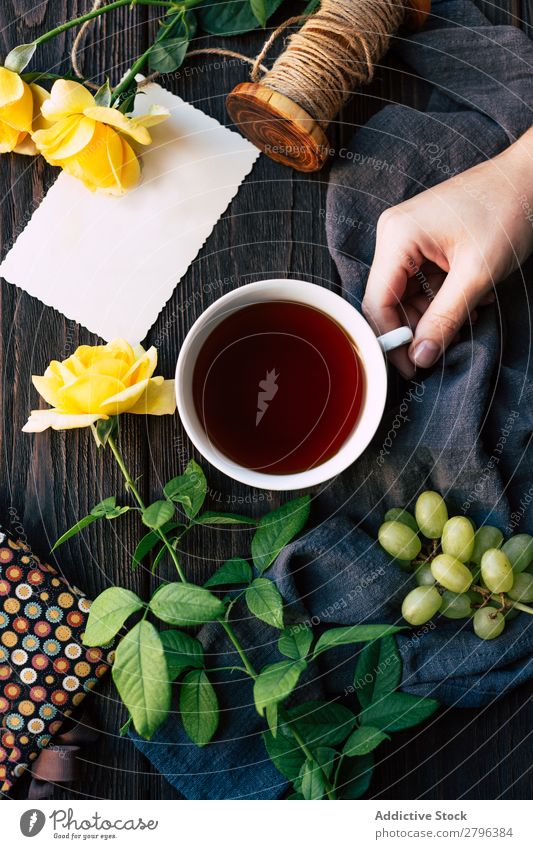 Getreidehand mit Tee in der Nähe von Blumen und leerer Note Hand Rose Hinweis blanko Tisch Stoff Weintrauben Faser Überraschung Geschenk Tasse trinken Getränk