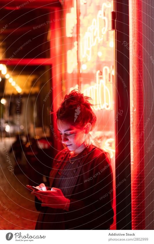 Attraktive, stylische Dame mit Smartphone in der Nähe von Neonröhren. Frau Stil PDA trendy neonfarbig Tel Aviv Israel Handy Schickimicki Straße Ohrringe Licht