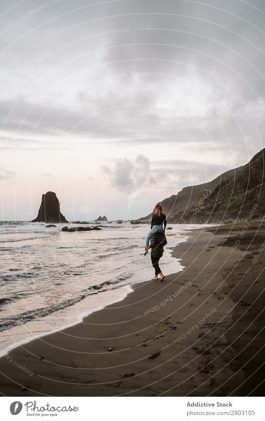 Nicht erkennbarer Mann, der eine Frau auf den Schultern nahe dem Meer trägt. Paar Huckepack Küste Zusammensein Sand Wolken Himmel Liebe Ferien & Urlaub & Reisen