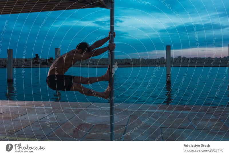 Sportlicher Mann balanciert auf der Stange am Ufer. Sportler Gleichgewicht Pfosten Stauanlage ohne Hemd Himmel Wasser Großstadt erstaunlich Abend sportlich