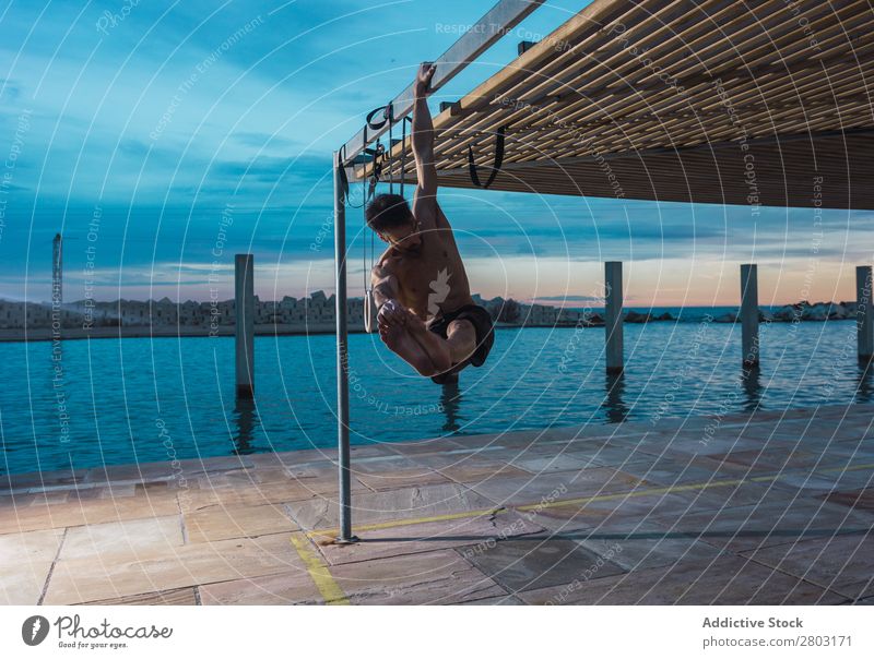 Athletischer Mann balanciert auf Gymnastikringen Sportler Gleichgewicht gymnastisch Stauanlage Ring ohne Hemd Wasser Großstadt Abend sportlich Jugendliche