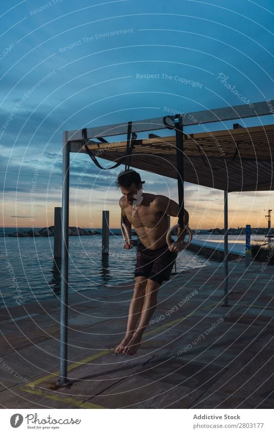 Athletischer Mann balanciert auf Gymnastikringen Sportler Gleichgewicht gymnastisch Stauanlage Ring ohne Hemd Wasser Großstadt Abend sportlich Jugendliche