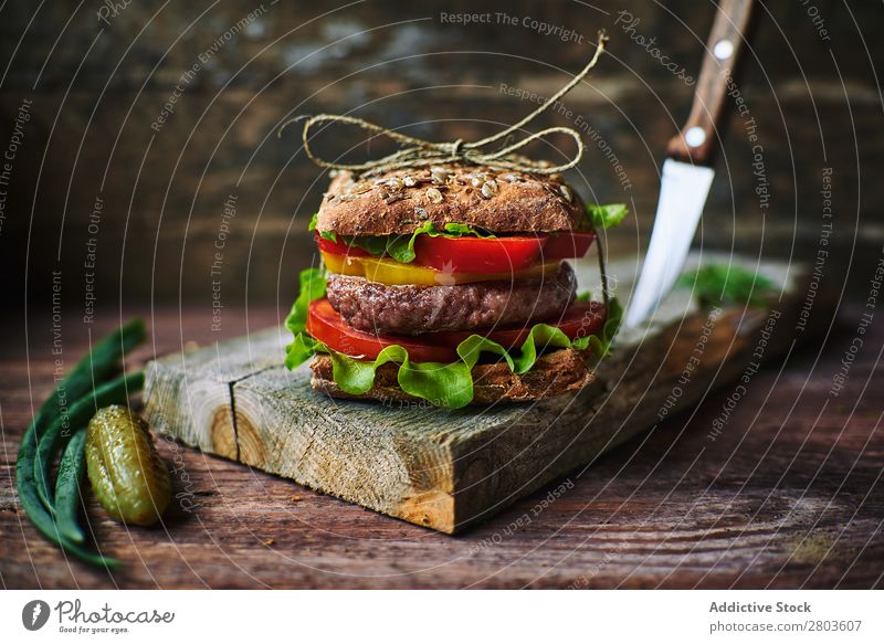 Köstlicher Burger auf Holzplatte Lebensmittel Zwiebel Senfgurke Vorbereitung Mittagessen Essen zubereiten Mahlzeit Brötchen Geschwindigkeit Feinschmecker