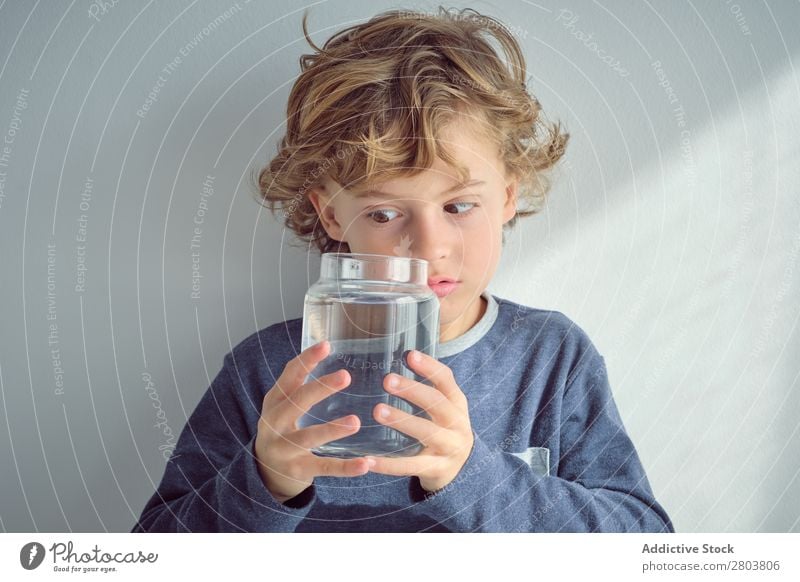 Junge hält Vase mit Wasser in der Nähe des Gesichts. Sauberkeit durchsichtig heimwärts Wand weiß lässig Kind Reinheit anschaulich frisch heiter Freude Glück