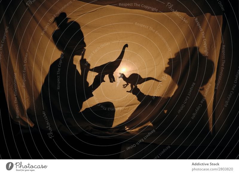 Silhouette einer Frau mit einem Kind, das hinter dem Laken spielt. Spielen Schatten Wohnung Dinosaurier Illumination Freude Zusammensein Abend Nacht Mutter