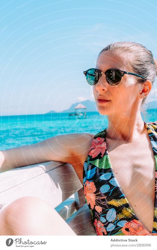 Frau im Bikini sitzt auf einer Bank in der Nähe des Wassers. Meer Jamaika Sonnenbrille Badeanzug Sitz blau tropisch exotisch sitzen Accessoire Sommer dünn Dame