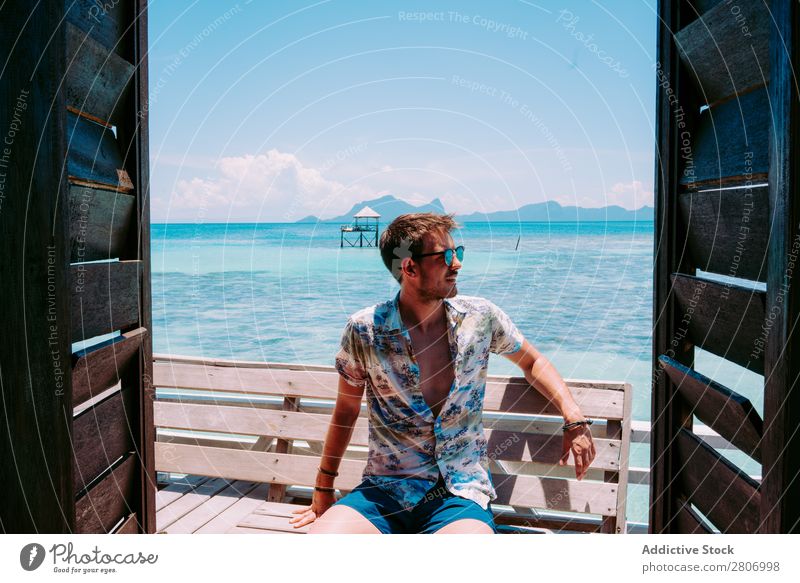 Mann mit Sonnenbrille sitzt auf einer Bank in der Nähe des Wassers. Meer Jamaika Sitz blau tropisch exotisch sitzen Jugendliche aussruhen Accessoire Sommer Typ