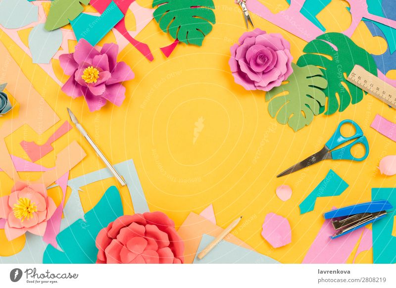 Papierbedarf und Papierblumen auf gelbem Hintergrund blau Farbe rosa Feiertag Schreibstift Teppichmesser Heftklammerer Lineal Schere geschnitten Gänseblümchen