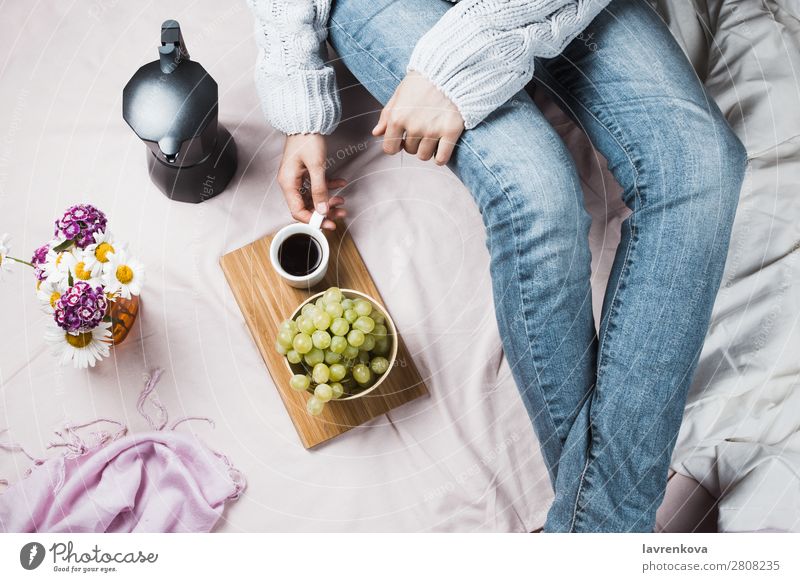 Frau in Jeans und Pullover im Bett mit Kaffee und Trauben schön Bettwäsche Decke Bettdecke Blumenstrauß Frühstück Cafétier Korbblütengewächs Gänseblümchen Diät