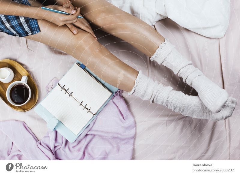 Weißgebräunte Frau in weißen Socken, die in ihrem Bett sitzt. gemütlich Winter Herbst flache Verlegung Hygge Erwachsene Einsamkeit schön Bettwäsche Decke
