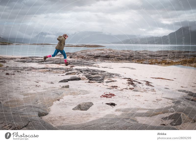 Junge Frau springt am Strand vor norwegischem Küstenpanorama Ferien & Urlaub & Reisen Abenteuer Ferne Freiheit Insel Jugendliche Natur Wolken Berge u. Gebirge